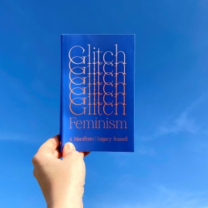 A hand is holding the book Glitch Feminism up to the sky
